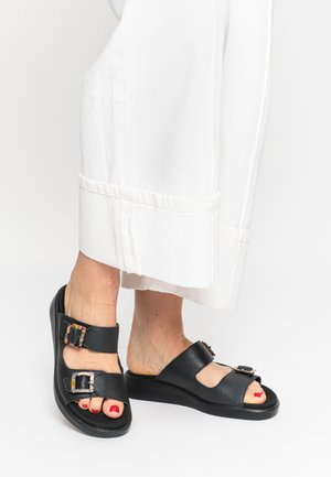 Black leather slide sandals with two adjustable straps and rectangular buckles, featuring an open toe and a thick, textured sole.
