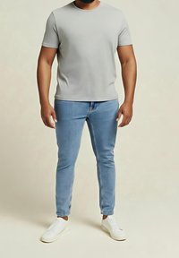 Šedé tričko s krátkým rukávem spárované s úzkými světlomodrými džínami a bílými teniskami. Materiál působí hladce s pohodlným střihem.