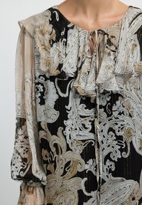 Blusa nera con intricati motivi floreali bianchi e dorati, caratterizzata da un colletto arricciato e maniche ampie e trasparenti. Tessuto morbido e leggero.
