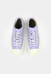 Lavender canvas sneakers with white rubber toe caps, metal eyelets, and flat laces. Interior features brand logo. Classic design with low profile.