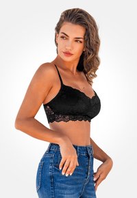 Bralette de encaje negro con tirantes ajustables, patrón floral texturizado y diseño recortado que acentúa el detalle del dobladillo de encaje.