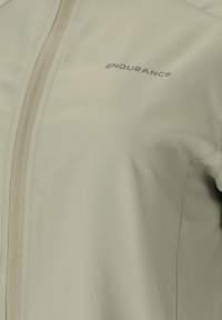 Light beige jacket with a vertical zipper on the left and "ENDURANCE" printed in small letters on the chest.