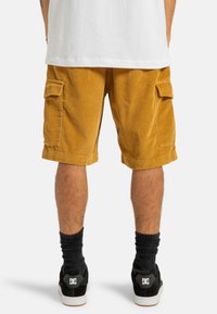 Kordfløjs cargo shorts i sennepsgul, med sidelommer og en afslappet pasform, parret med sorte sneakers og ribbede sokker.