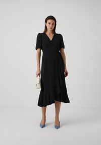 Black wrap dress with short puff sleeves, a V-neck, and ruffle hem, paired with light blue pointed pumps and a small white handbag.