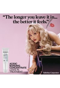 Donna bionda con capelli mossi si appoggia a un pianoforte, accanto a un tubo del trattamento leave-in Redken Acidic Bonding Concentrate e a una citazione del prodotto.