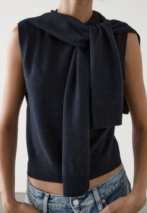 Marineblauwe mouwloze trui met een gedrapeerde halsdetail, gemaakt van zacht materiaal; gecombineerd met hoge tailles denim shorts met een lichte wassing.