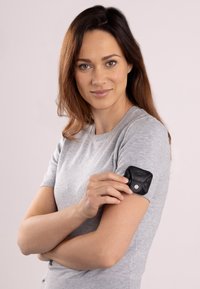 Schwarzes Lederaccessoire, das an einem grauen kurzärmeligen Pullover mit einem sicheren Druckknopf befestigt ist. Glatte Textur und feine Nähte sind sichtbar.