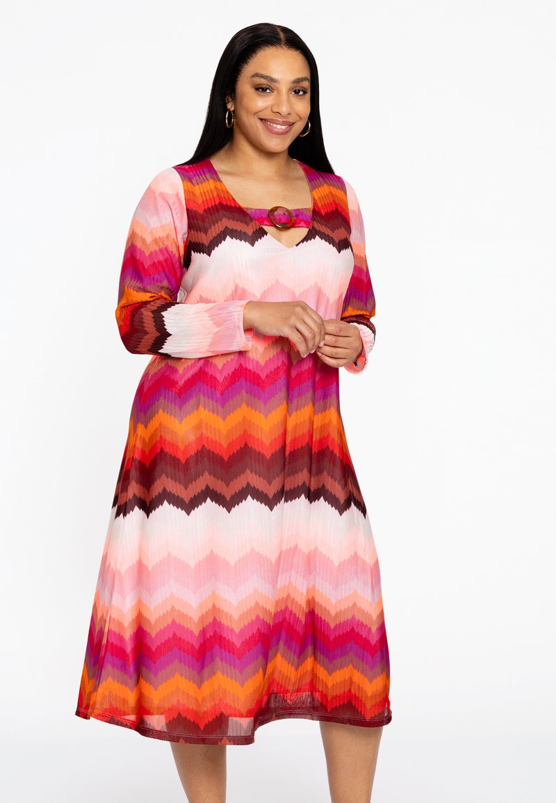 Farbiger Chevron-Musterkleid in Pink, Orange und Braun, mit einem V-Ausschnitt und einem dekorativen runden Akzent an der Brust. Lange Ärmel.