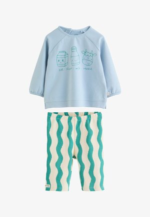 Haut à manches longues bleu clair pour tout-petit avec un carton de lait, une bouteille et une vache dessinés en cartoon, associé à un pantalon rayé ondulé crème et bleu sarcelle.