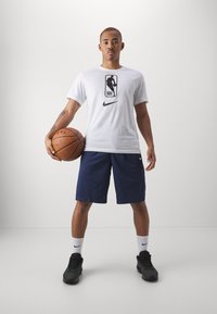 Valge NBA-logo t-särk ümmarguse kaelusega, koos tumesiniste korvapalli lühikeste pükstega. Figuur hoiab pruuni korvpalli ja kannab musti spordijalatsi.