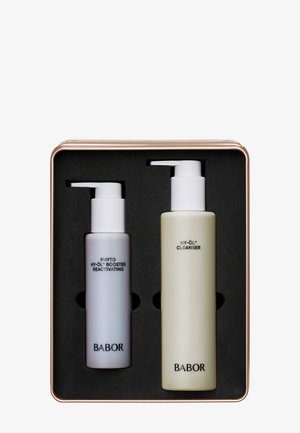 Set aus zwei Hautpflegeflaschen: ein hoher, mintgrüner Reiniger und ein kürzerer grauer Booster, beide mit weißen Pumpspendern, in einer roségoldenen Dose mit schwarzem Schaum.