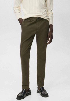 Dark olive green tailored pants made of smooth fabric, featuring a straight cut and front pockets, paired with black loafers.
