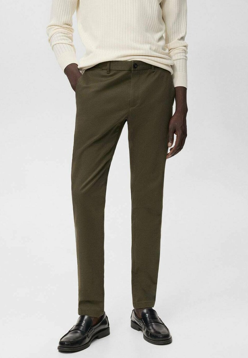 Dark olive green tailored pants made of smooth fabric, featuring a straight cut and front pockets, paired with black loafers.
