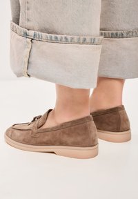Lichtbruine suède loafers met een moccasin ontwerp, met een instapstijl en een tan rubberen zool. Zichtbare stiksels langs de randen.