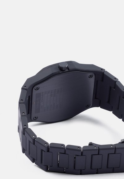 Čierne analógové hodinky s matným povrchom, oktágonaľným puzdrom, hladkým remienkom s obdĺžnikovými článkami a textúrovaným zadným dielom so vygravírovanými špecifikáciami.