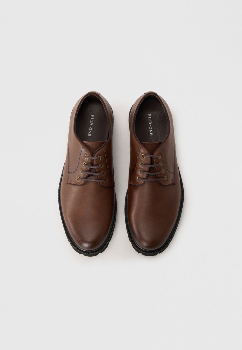 Zapatos de cuero marrón con un acabado suave, que cuentan con seis ojetes, cordones de tono bronce y una suela de goma negra texturizada.