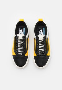 Tênis pretos e amarelos com uma mistura de couro e lona, apresentando uma biqueira branca, atacadores proeminentes e uma etiqueta de marca na lingueta.