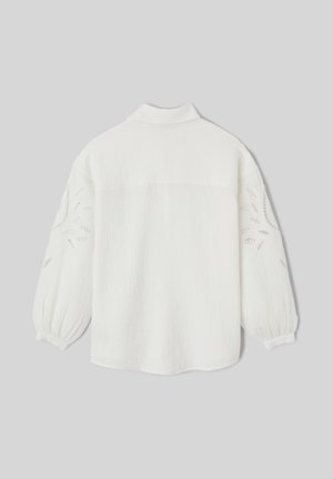 Blouse blanche à manches longues avec manches bouffantes et motifs floraux découpés sur les bras, présentée de dos sur un fond gris.