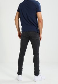 Camiseta de manga corta azul marino combinada con jeans negros de corte ajustado y zapatillas blancas, con diseño de bolsillo estándar y detalles simples de costura.