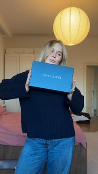 Plavi pravokutni okvir s natpisom "PIER. ONE" zlatnim slovima. Model u tamnoplavom džemperu i plavim trapericama drži okvir u visini prsa.