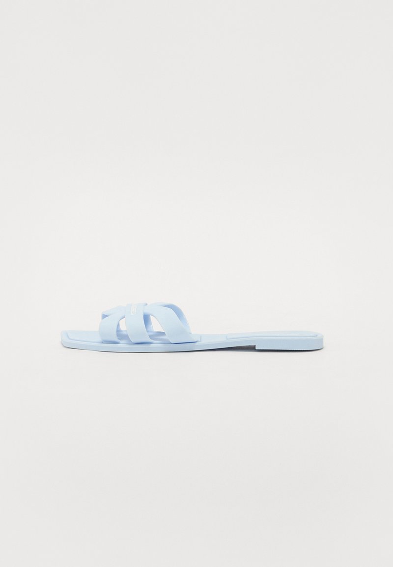Blå platta sandaler gjorda av slät plast med korsade remmar; rektangulär sula, minimal design och platt profil.