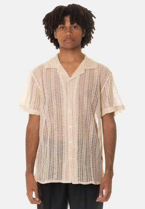 Camicia a maniche corte con bottoni di un leggero beige, caratterizzata da un design testurizzato a maglia aperta, colletto e dettagli di cucitura eleganti.