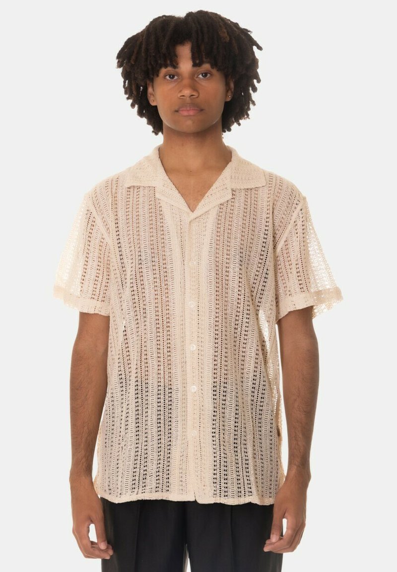 Camicia a maniche corte con bottoni di un leggero beige, caratterizzata da un design testurizzato a maglia aperta, colletto e dettagli di cucitura eleganti.