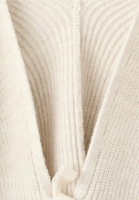 Gros plan sur un tissu blanc en tricot avec une texture douce et côtelée, une section pliée créant une forme en V au centre.