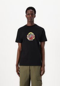 Black cotton t-shirt with a colorful graphic featuring a skeleton and a sombrero at the center, paired with olive green cargo pants.