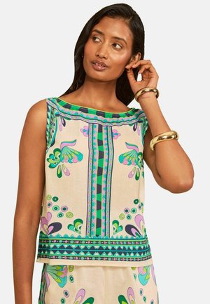 Kvinde iført en ærmeløs beige top med grønne, lilla og blå blomster- og geometriske mønstre samt to gyldne armbånd på hendes håndled.