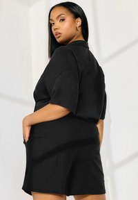 Ensemble court en lin noir avec des manches courtes et une coupe décontractée. Comprend des poches latérales et un col simple, mettant en avant un design minimaliste.