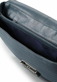 Borsa a tracolla in pelle blu con cuciture visibili, apertura superiore che mostra l'interno in tessuto scuro e chiusura rettangolare in argento sulla parte frontale.