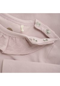 Helles rosa Baumwollkleidungsstück mit einem strukturierten, gerüschten Kragen, silbernen Druckknöpfen und sauberer Nahtdetail. Weiche, glatte Textur.