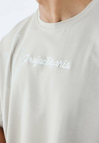 Camiseta de color gris claro hecha de tela suave, con texto bordado "Projectparis" y un dibujo a línea de un cactus en el lado izquierdo.