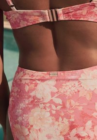 Bloem bikini top en bottom in tinten van roze, met grote witte bloemen en een zachte textuur. Hardware details op de bandjes en de tailleband.