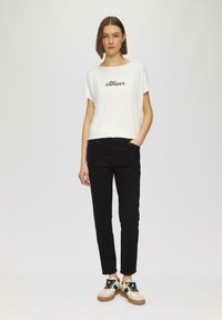 T-shirt blanc à manches courtes avec "s.Oliver" imprimé en noir, associé à un pantalon noir slim et des baskets multicolores à semelle épaisse.