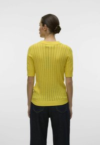 Geel gebreid sweatshirt met korte mouwen, voorzien van een textuur, geribbelde afwerking en een open stekenpatroon. Afgewerkt met een ronde halslijn.