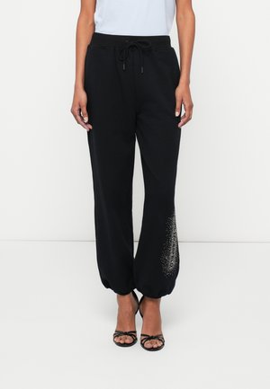 Fekete melegítőnadrág, szűkített lábszárral, állítható zsinóros derékkal és díszítő mintázattal, amely apró fémes pöttyökből áll az alsó lábszáron.