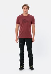 Rood gemarmerd T-shirt met korte mouwen en een bergafbeelding, gecombineerd met zwarte broeken met gestructureerde knieaccenten en zwarte schoenen.