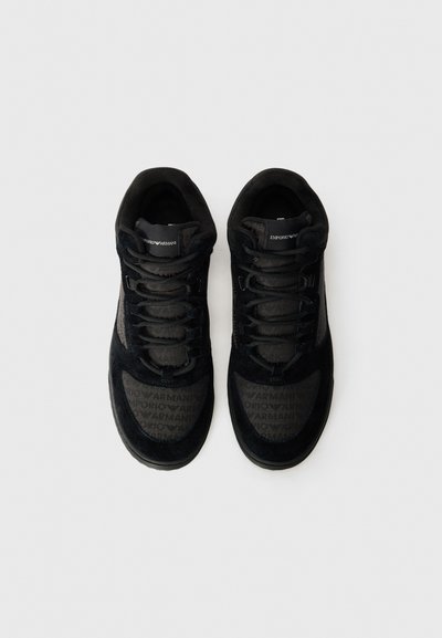 Baskets noires en suède avec des accents en mesh, présentant un design texturé et des détails de logo sur les côtés et la languette.