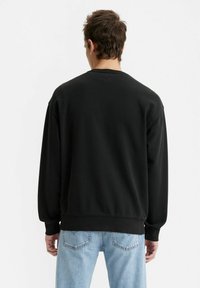 Zwarte sweatshirt met een ronde hals, verlaagde schouders en geribbelde manchetten. Gekenmerkt door een minimalistisch ontwerp zonder zichtbare logo's, gedragen met lichtblauwe jeans.