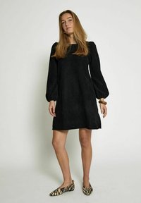 Black corduroy dress with long puff sleeves, featuring a square neckline. Worn with zebra print flats and a wooden bracelet.