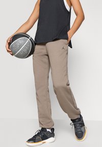 Beige sweatpants med slim fit og en liten svart logo. Svart tank top og grå joggesko med gule detaljer. Basketball i hånden.