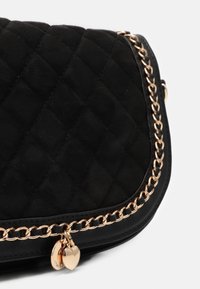 Borsa in suede nera trapuntata con dettagli in catena dorata e ciondoli a forma di cuore. Presenta un design elegante con una finitura testurizzata.