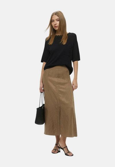 Top nero a maniche corte, gonna midi marrone con uno spacco laterale e tasca frontale, e sandali neri con cinturini. Tiene una borsa a tracolla intrecciata nera.