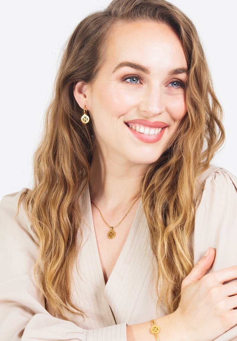 Gouden juwelenset met een hangerketting, oorringen en een armband, elk met een cirkelvormig charmeontwerp en een gepolijste afwerking.