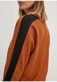 Jersey naranja con un acabado texturizado, que cuenta con una franja vertical negra en el hombro. Diseño sencillo y ajuste cómodo.