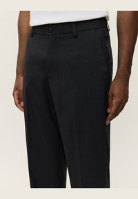 Dunkelgraue, maßgeschneiderte Hosen mit einer glatten Textur, die einen Frontknopfverschluss, Gürtelschlaufen und schräge Seitentaschen aufweisen.
