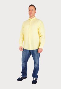 Camicia a maniche lunghe gialla chiaro con bottoni, dal taglio morbido, abbinata a jeans in denim blu e scarpe navy con dettagli bianchi.