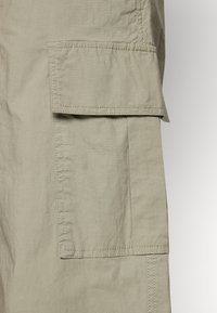 Khaki cargo šortky s velkou boční kapsou s klopou, prošívanými detaily, lehkým materiálem a volným střihem.